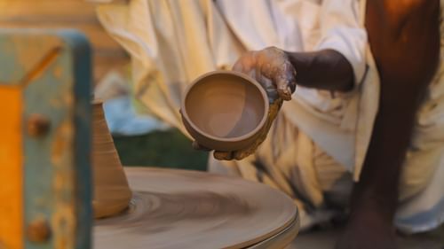 A man doing pottery and holding a small clay bowl he made